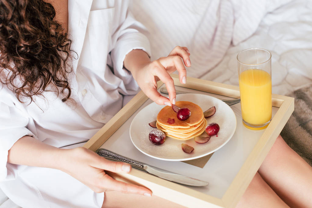 partial view of curly woman having breakfast in bed - Photo, Image