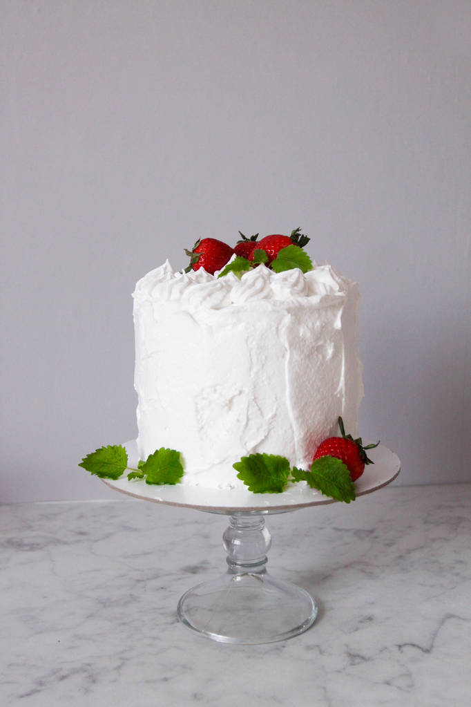 Suuri valkoinen herkullinen kakku kermalla ja koristeltu mansikoilla ja mintulla läpinäkyvällä jalustalla harmaalla pohjalla
   - Valokuva, kuva