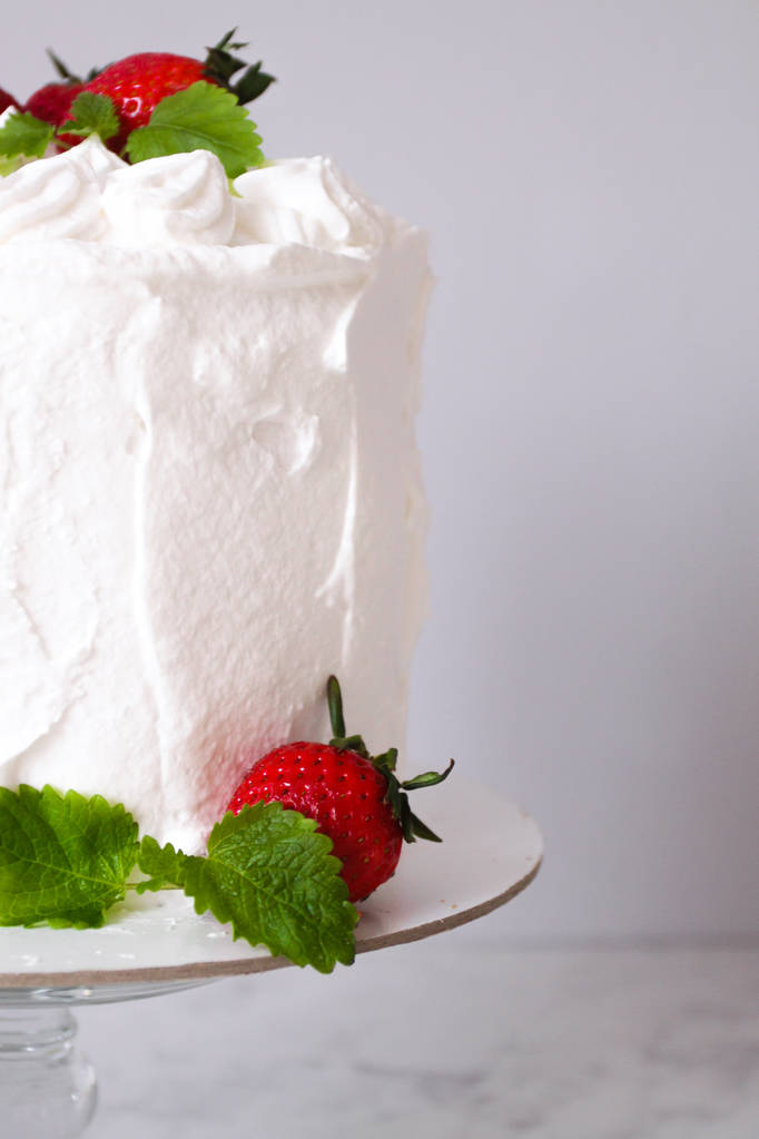 Suuri valkoinen herkullinen kakku kermalla ja koristeltu mansikoilla ja mintulla läpinäkyvällä jalustalla harmaalla pohjalla
   - Valokuva, kuva