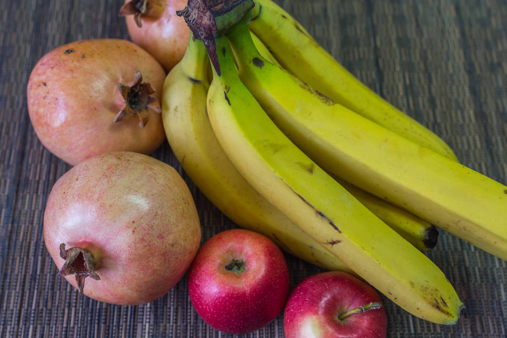 Composición de frutas sobre la mesa. Vida muerta de granadas, manzanas y plátanos de cerca
. - Foto, Imagen