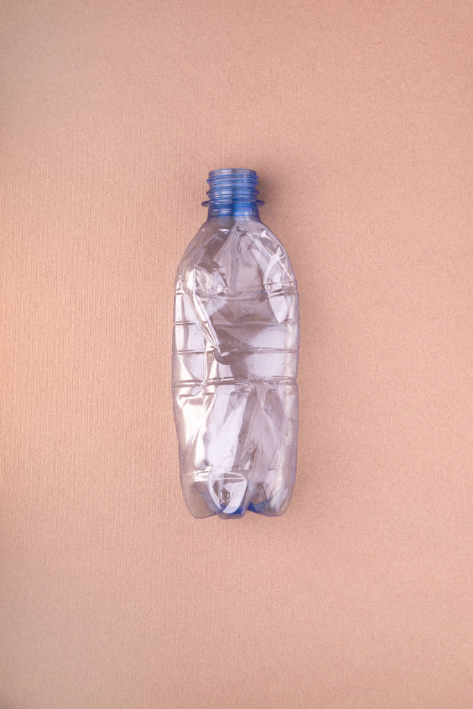 Crashed plastic bottle on beige tan background. Plastic utilisation concept. Ecological problem, global environment. - Photo, Image