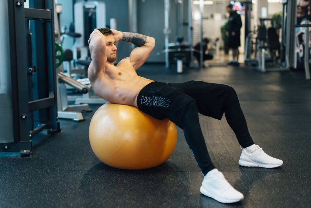 Homem muscular jovem treina músculos abdominais usando bola de exercício
 - Foto, Imagem