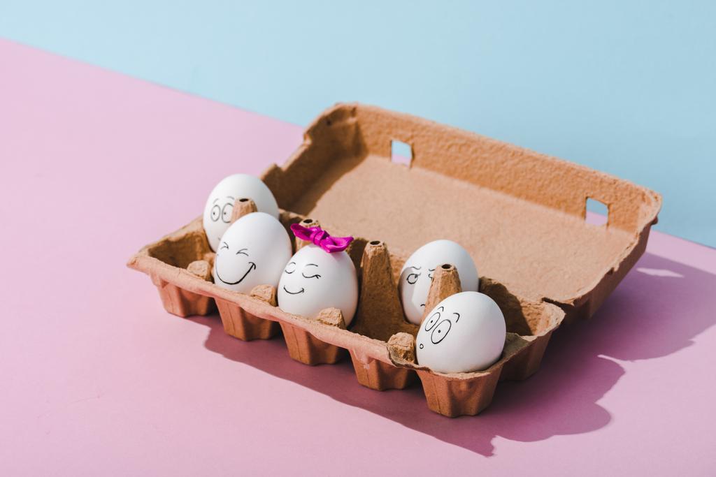 huevos con varias expresiones faciales en cartón de huevo en azul y rosa
 - Foto, imagen