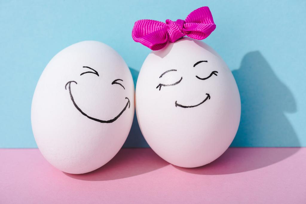 αυγό με τόξο και αυγό με ευτυχισμένο πρόσωπο έκφραση σε μπλε και ροζ - Φωτογραφία, εικόνα