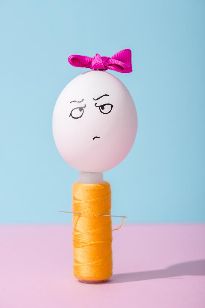 αυγό με τόξο και θυμωμένη έκφραση προσώπου στο πηνίο νήματος στο μπλε και ροζ - Φωτογραφία, εικόνα