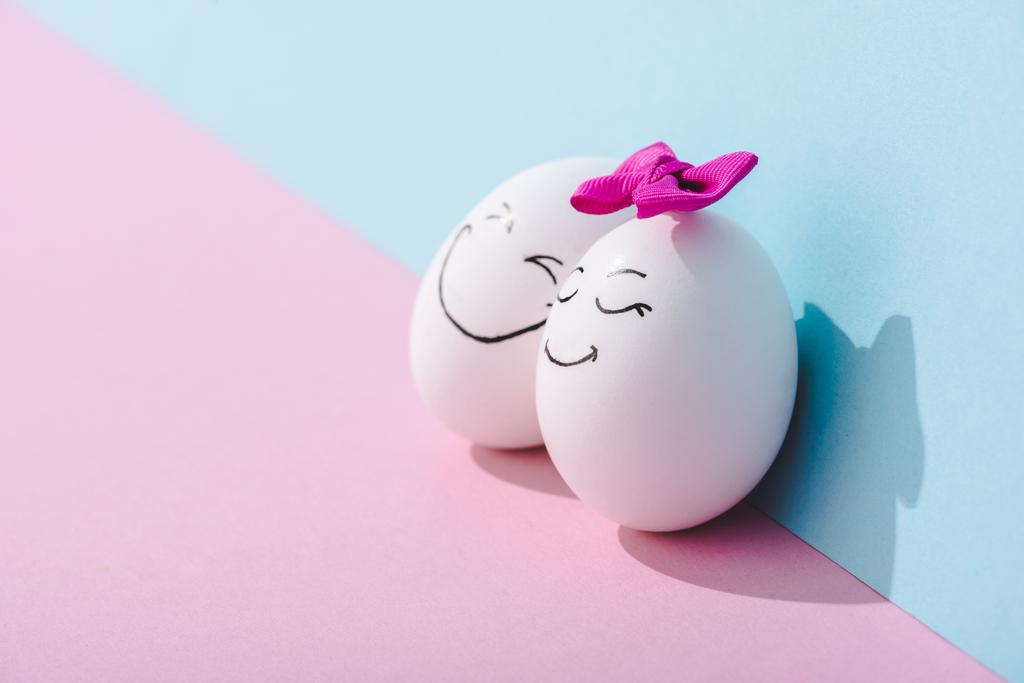 αυγό με τόξο και αυγό με ευτυχισμένο πρόσωπο έκφραση στο μπλε και ροζ με χώρο αντιγραφής - Φωτογραφία, εικόνα