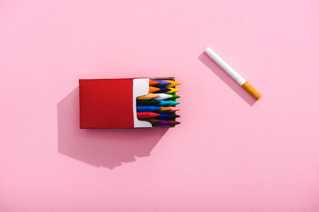 vista superior de lápices de colores en el paquete de cigarrillos y el cigarrillo de tabaco en rosa, concepto de fumar
 - Foto, imagen