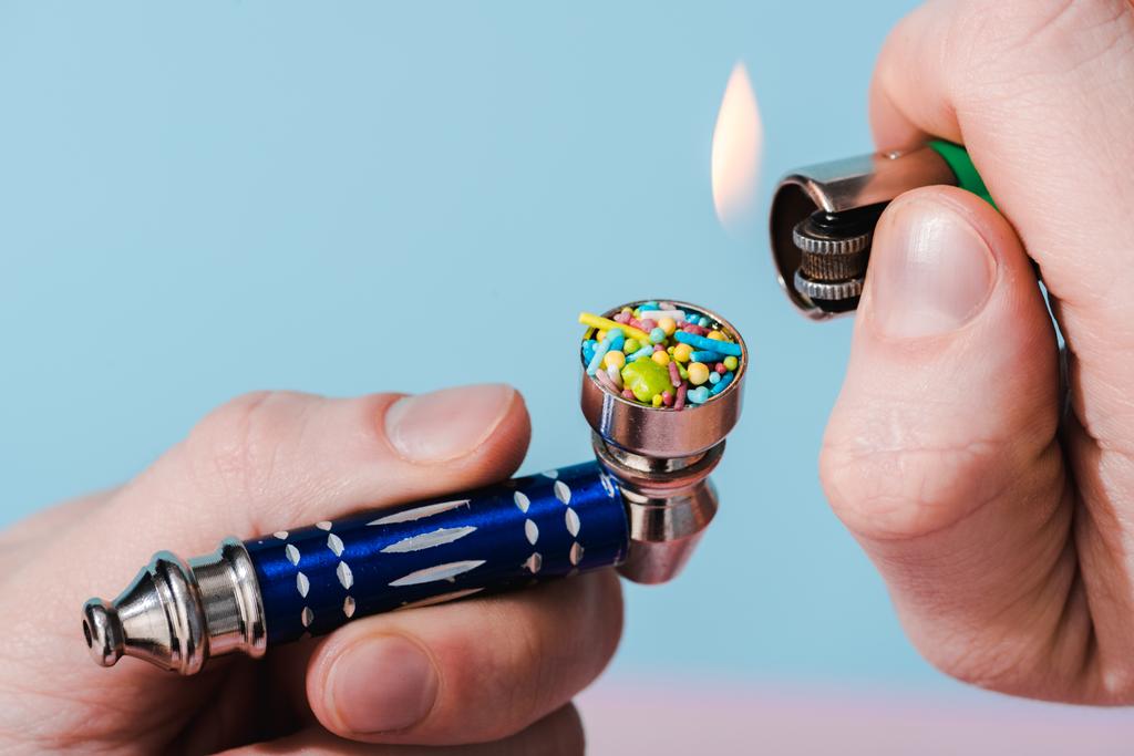 Περικομμένη όψη του ανθρώπου φωτισμός κάπνισμα σωλήνα με πολύχρωμες τρούφες στο μπλε, έννοια εθισμός στην ζάχαρη  - Φωτογραφία, εικόνα