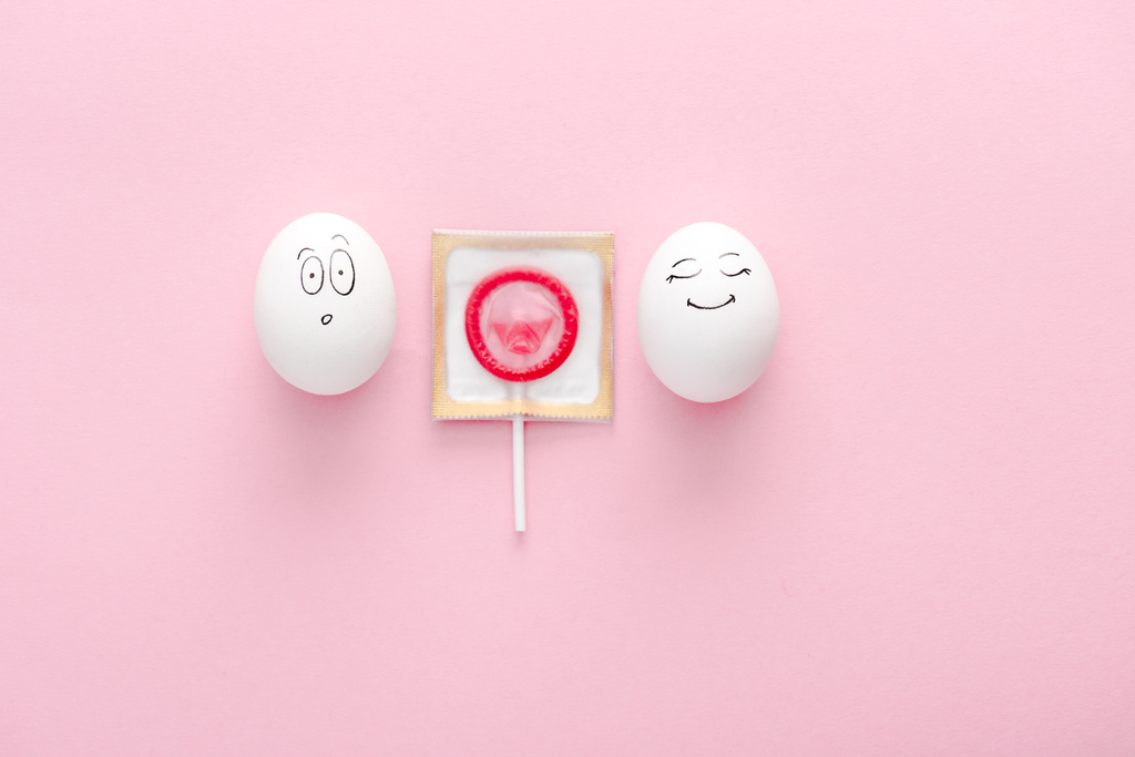 Ansicht von Eiern mit glücklichen und überraschten Gesichtsausdrücken mit Kondom als Lutscher auf rosa mit Kopierraum - Foto, Bild