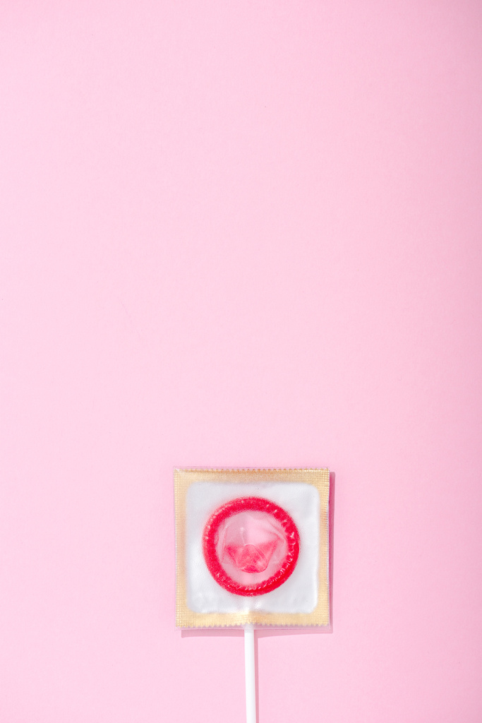 κορυφή θέα του προφυλακτικού τυλιγμένο ως γλειφιτζούρι σε ροζ με αντίγραφο χώρου, ασφαλής σεξ ιδέα - Φωτογραφία, εικόνα