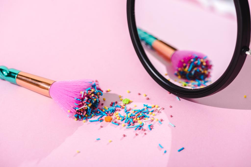 pincel de maquillaje cubierto de coloridos espolvoreos con reflejo en espejo sobre rosa
 - Foto, imagen