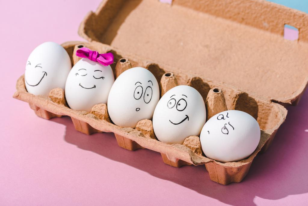 αυγά με διαφορετικές εκφράσεις προσώπου σε κουτί αυγών σε ροζ - Φωτογραφία, εικόνα
