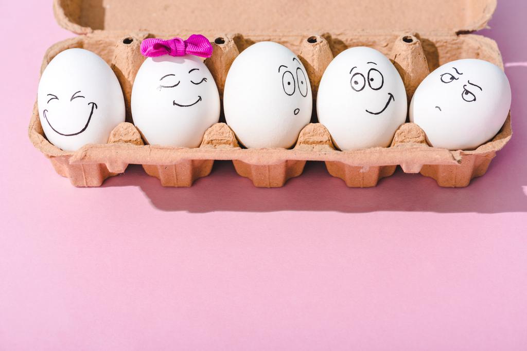 eggs with different face expressions in egg carton on pink with copy space - Photo, Image