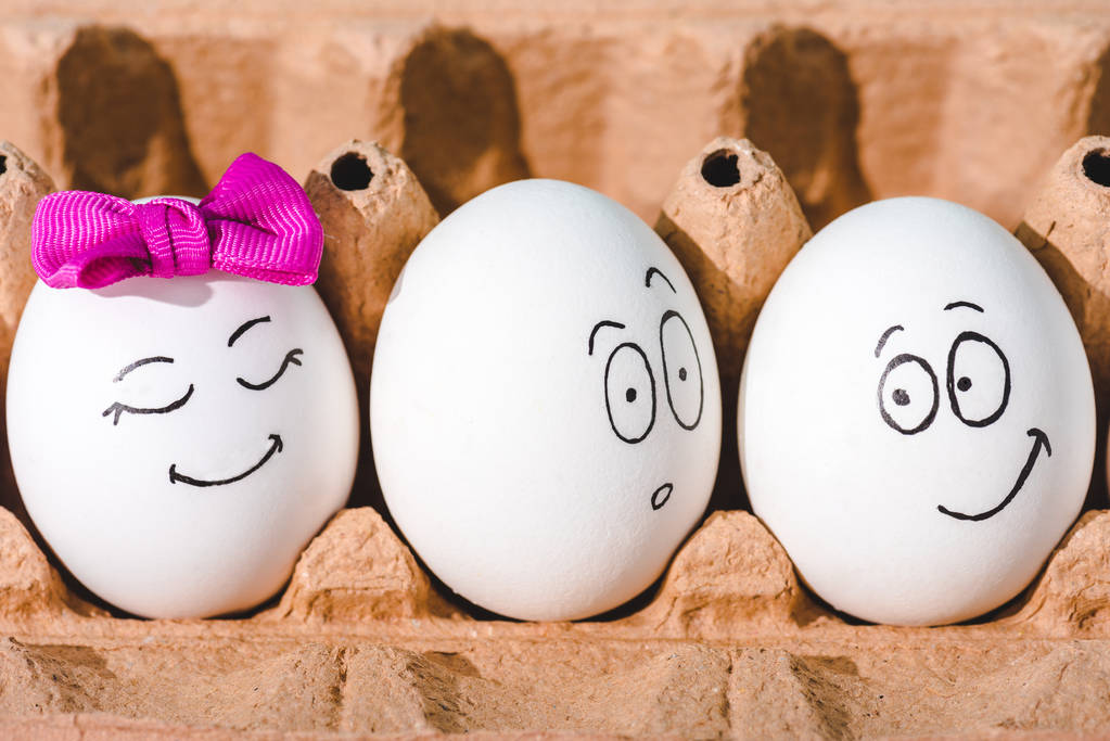 Close-up van eieren met glimlachende en geschrokken gezichtsuitdrukkingen in eier karton  - Foto, afbeelding