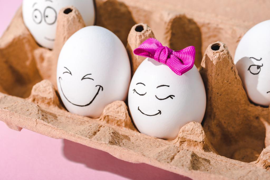 eieren met verschillende gezichtsuitdrukkingen in eier karton op roze - Foto, afbeelding
