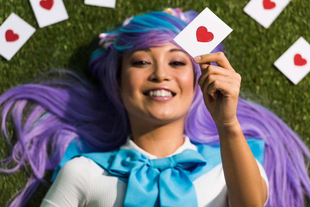 Selektywne skupienie azjatyckiego anime girl w purpurowej peruce karty i leżącej na trawie - Zdjęcie, obraz