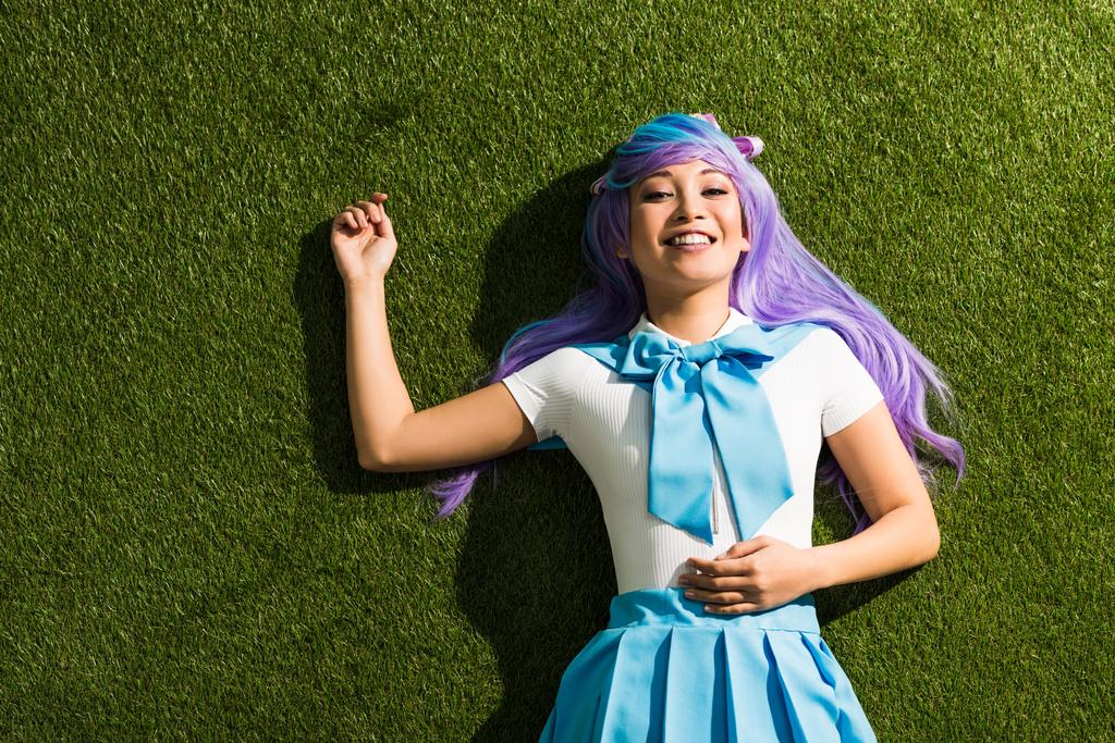 lächelnde asiatische Anime-Mädchen in lila Perücke auf grünem Gras liegend - Foto, Bild