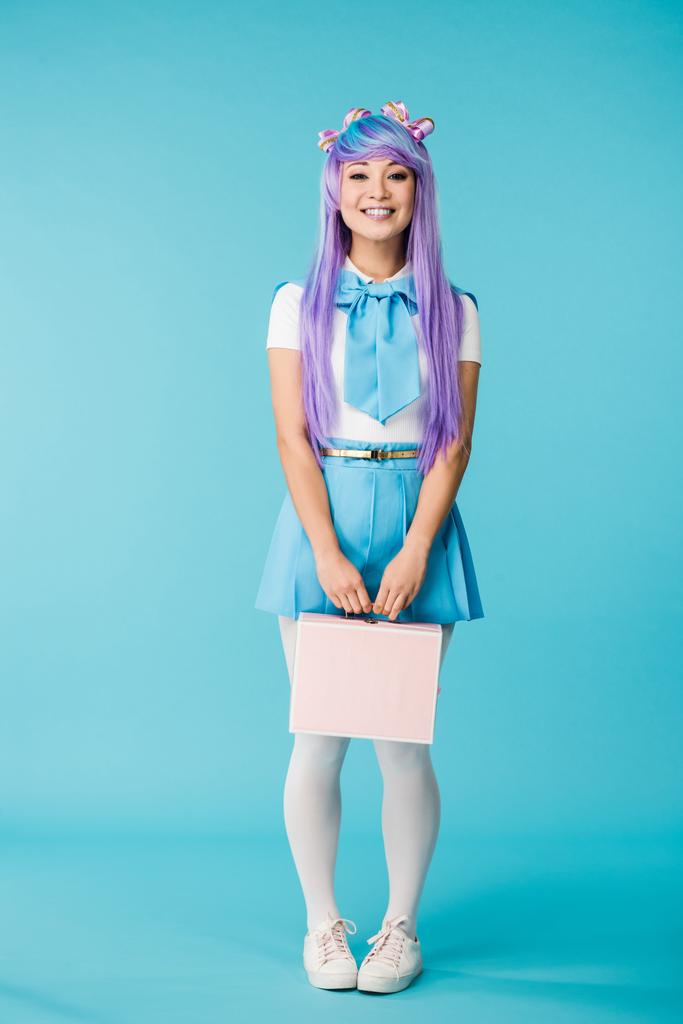 Vista completa de la chica anime en peluca púrpura celebración maletín en azul
 - Foto, Imagen