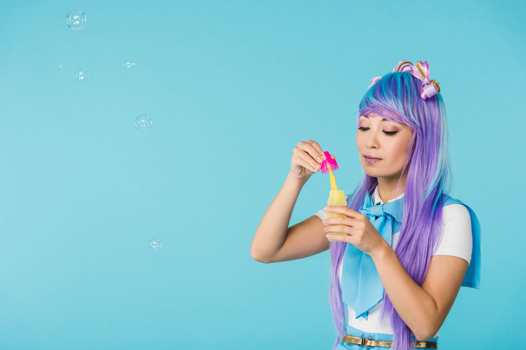 Chica anime asiático en peluca púrpura con burbujas de jabón aislado en azul
 - Foto, Imagen