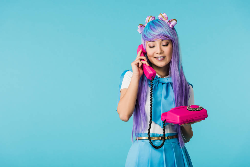 Smiling anime girl talking on telephone with closed eyes isolated on blue - Photo, Image