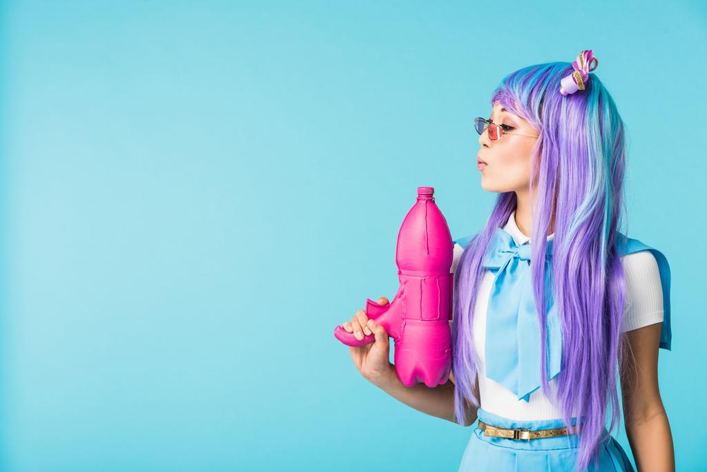 asiático anime chica en peluca y gafas celebración agua pistola aislado en azul
 - Foto, Imagen