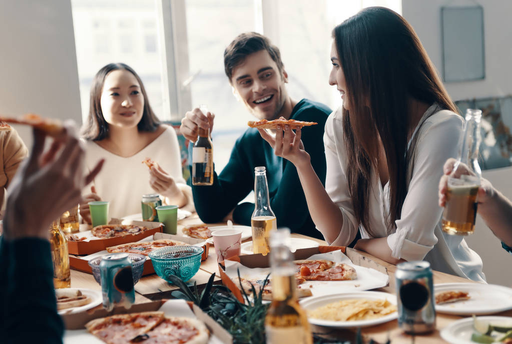 Bonne nourriture et bons amis. Groupe de jeunes en tenue décontractée mangeant de la pizza et souriant lors d'un dîner à l'intérieur
 - Photo, image
