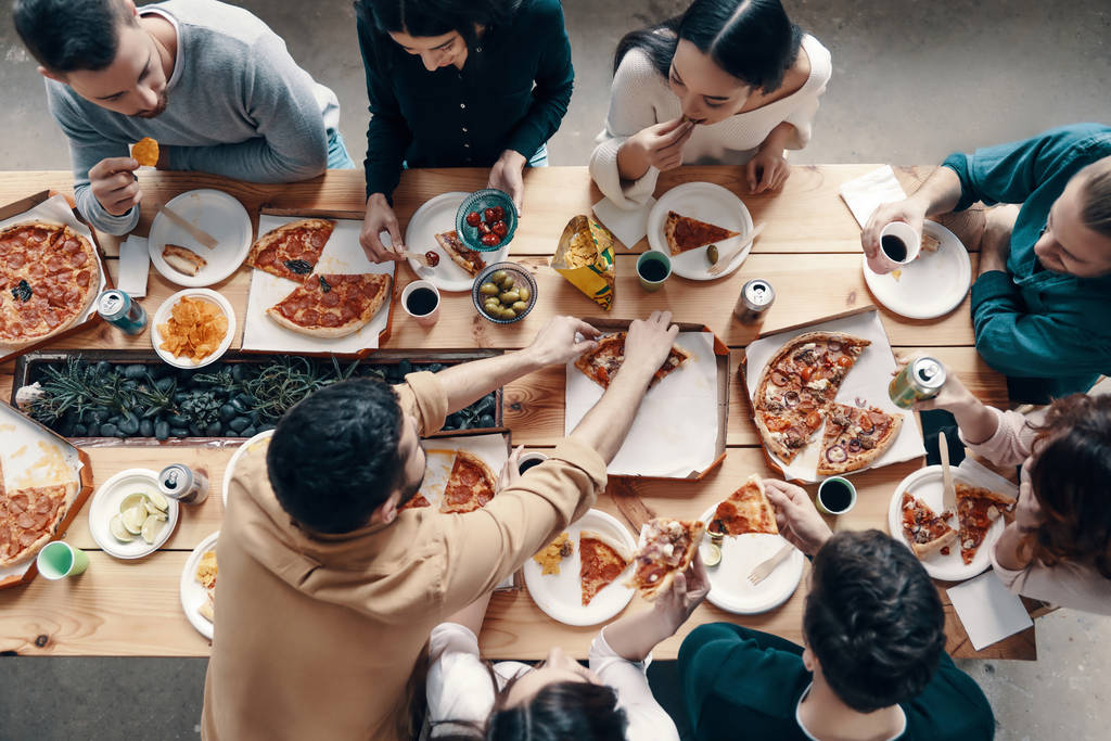 Вид зверху на молодих людей в повсякденному одязі збирання піци під час вечірки в приміщенні
 - Фото, зображення