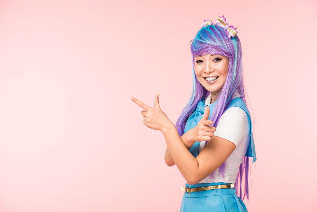 Chica animada alegre en peluca púrpura señalando con los dedos aislados en rosa
 - Foto, Imagen