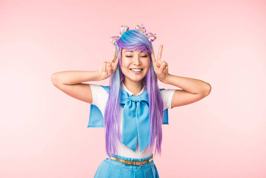 Šťastná anime dívka v purpurové paruce ukazující mírové znaky s zavřenýma očima na růžovém - Fotografie, Obrázek