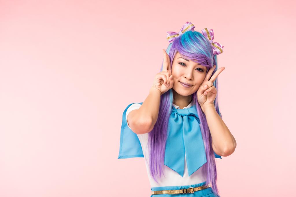 Mooie Aziatische anime meisje in paarse pruik tonen vrede tekenen geïsoleerd op roze - Foto, afbeelding