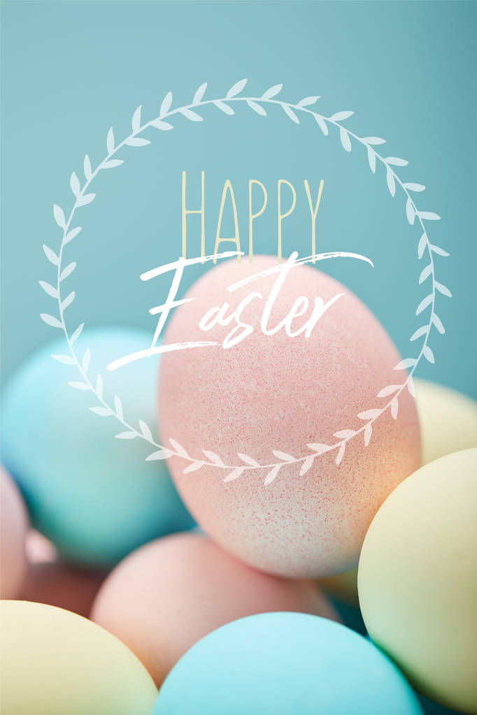 pile of multicolored painted chicken eggs with happy Easter lettering in circle on blue background - Photo, Image