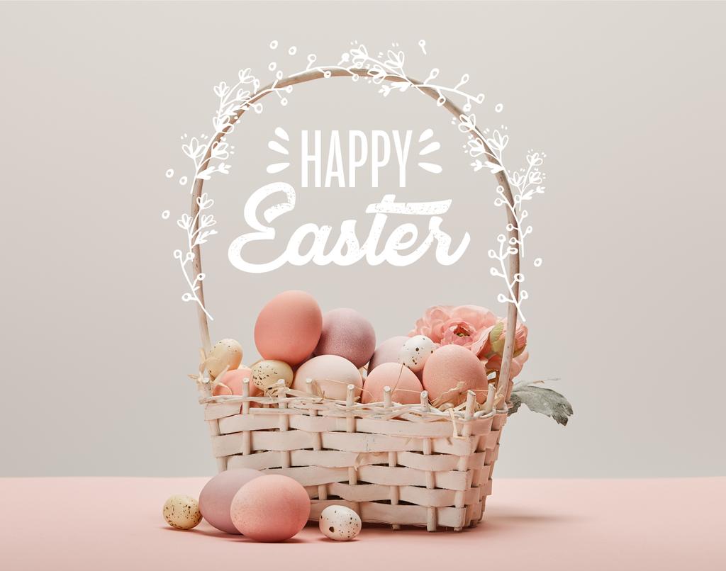 wicker basket with pink painted eggs, flowers and happy Easter lettering on grey background - Photo, Image