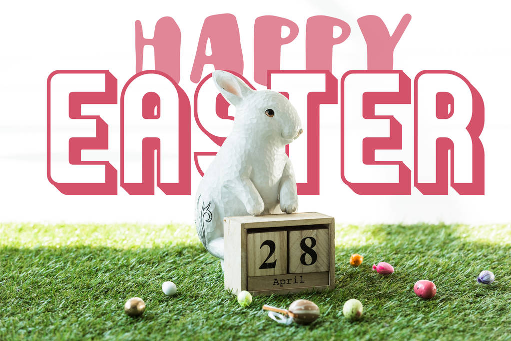 διακοσμητικό κουνέλι, ξύλινο ημερολόγιο με 28 Απριλίου ημερομηνία, και πολύχρωμα Πασχαλινά αυγά σε πράσινο γρασίδι με χαρούμενο Πάσχα γράμματα - Φωτογραφία, εικόνα