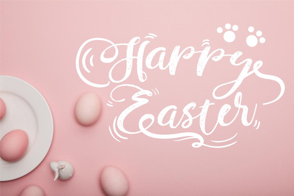 верхний вид покрашенных яиц и белого декоративного кролика возле тарелки на розовом фоне с радостным пасхальным надписью
 - Фото, изображение