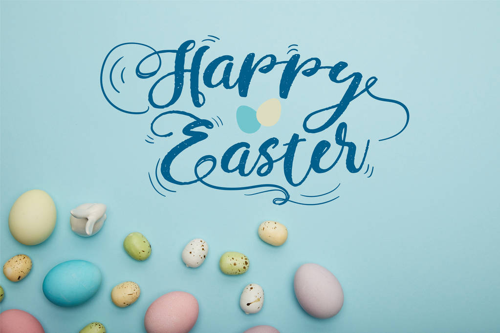 vue du dessus des œufs multicolores peints éparpillés près du lapin décoratif sur fond bleu avec un lettrage de Pâques heureux
 - Photo, image