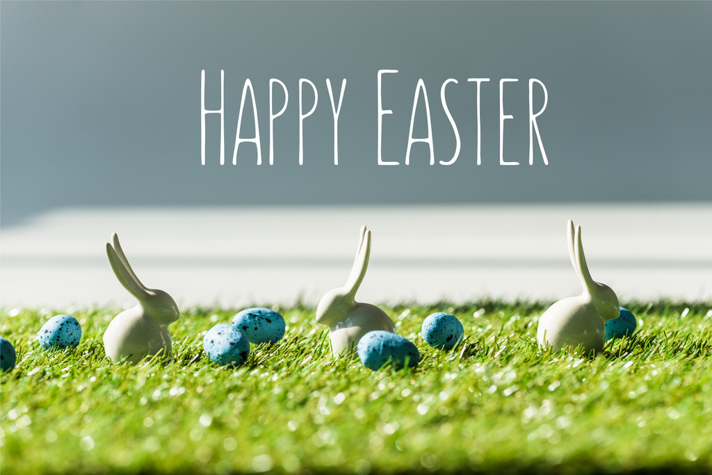 dekoracyjne króliki na zielonej trawie w pobliżu niebieskie Jaja przepiórcze z szczęśliwym wielkanocnym napisem - Zdjęcie, obraz