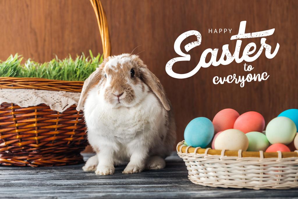 cute Bunny pobliżu wikliny kosze z zieloną trawą i kolorowe jaja kurze z Happy Wielkanoc dla wszystkich napis na drewnianym tle - Zdjęcie, obraz