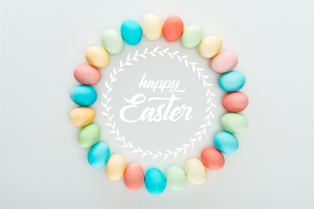 Top uitzicht van ronde frame gemaakt van geschilderde veelkleurige eieren met vrolijk Pasen witte belettering - Foto, afbeelding