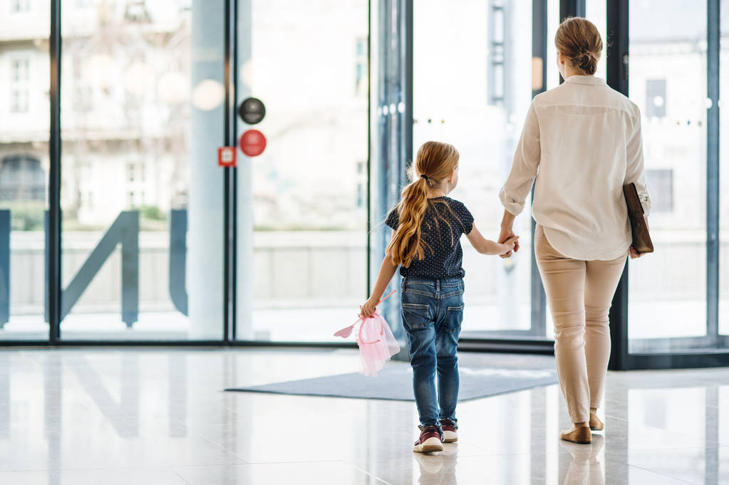 Une vue arrière d'une femme d'affaires avec une petite fille marchant dans un immeuble de bureaux
. - Photo, image