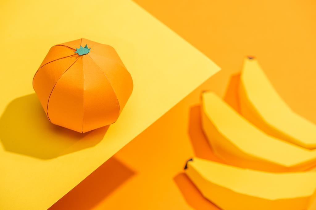 Επιλεκτική εστίαση του μανταρίνι οριγκάμι σε κίτρινο χαρτί με μπανάνες από χαρτόνι σε πορτοκαλί - Φωτογραφία, εικόνα