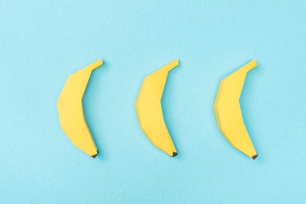 вид сверху на расположенные бананы из желтой бумаги, изолированные на голубом
 - Фото, изображение