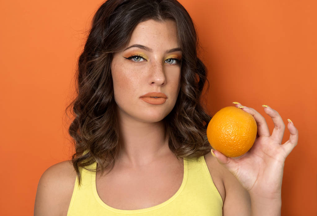 Mujer joven sosteniendo naranja sobre fondo brillante
 - Foto, Imagen