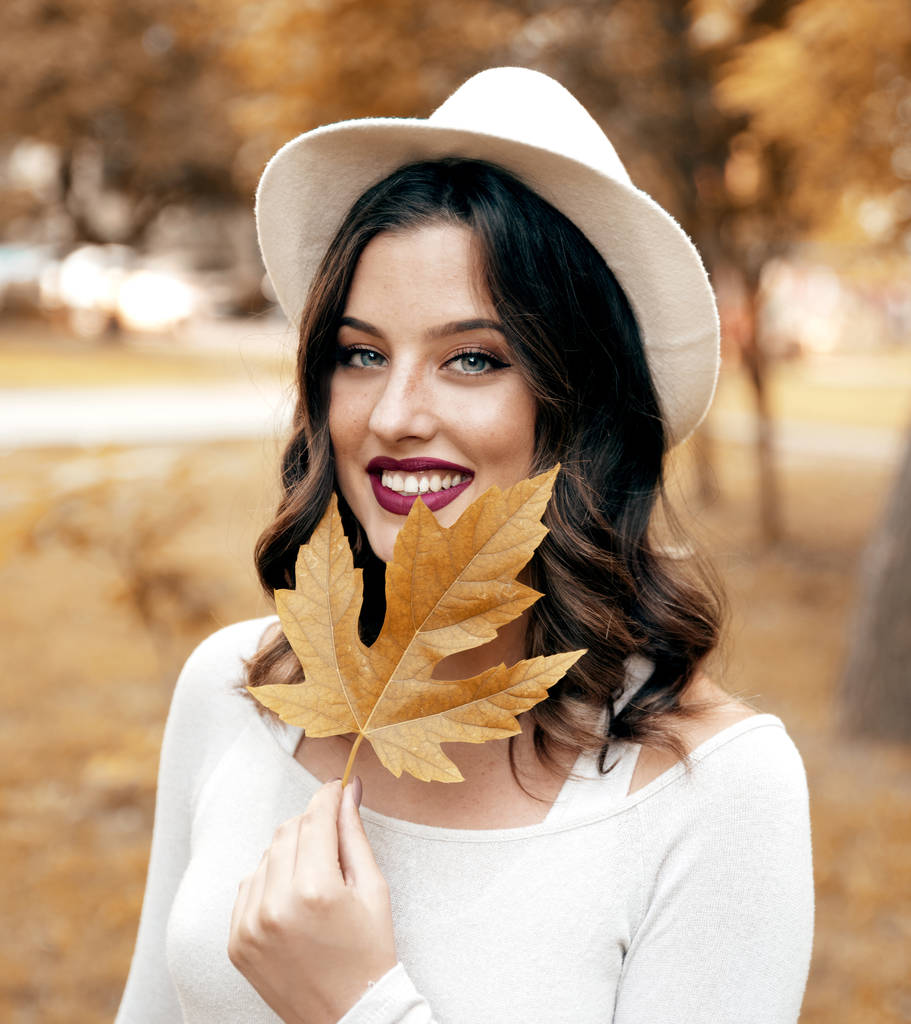 Mujer joven en sombrero sosteniendo hoja de otoño
 - Foto, imagen