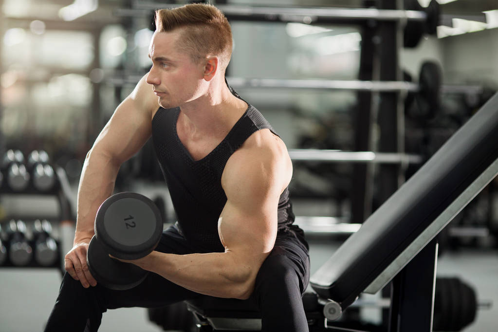 schöner Mann in guter Form mit Muskeln im Fitnessstudio, der Übungen mit Hanteln macht - Foto, Bild