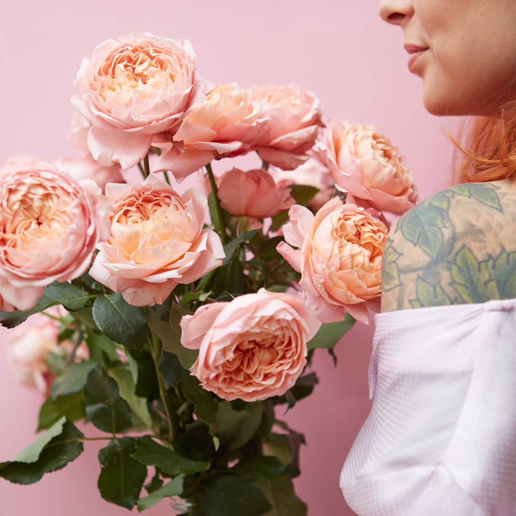 Un gran ramo de rosas rosadas frescas sostiene a una chica pelirroja con un tatuaje sobre un fondo rosado. Regalo de San Valentín
 - Foto, Imagen