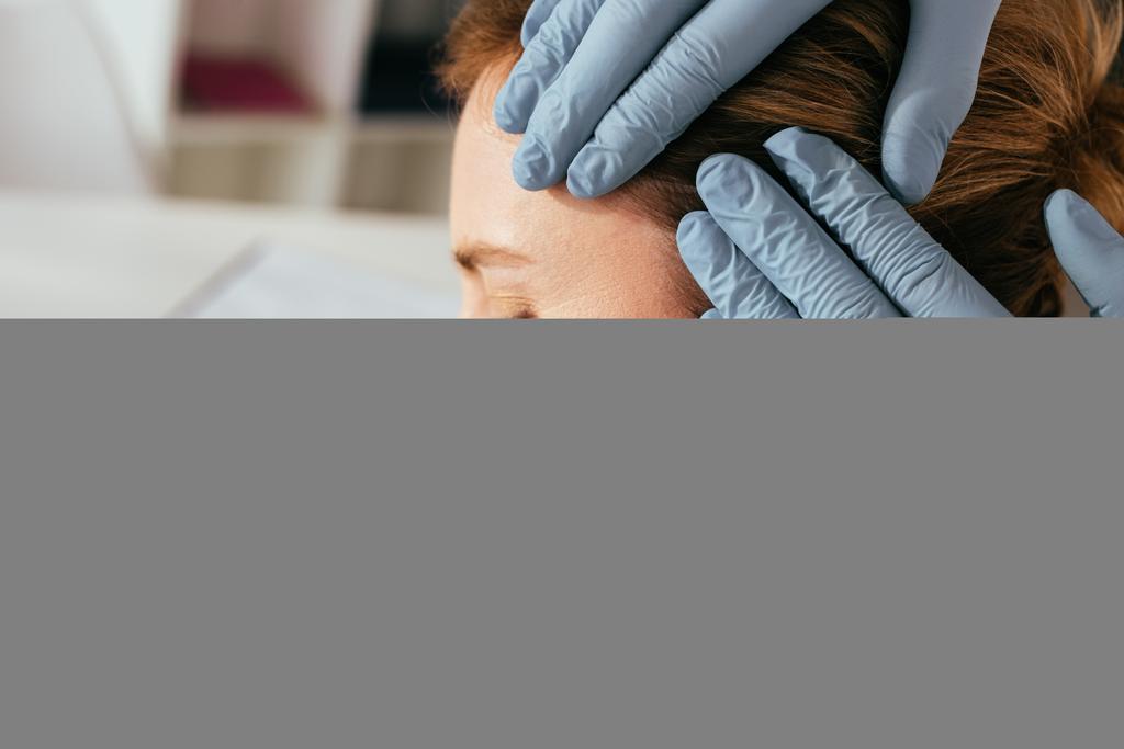 cropped view of dermatologist in latex gloves examining hair of attractive patient in clinic  - Photo, Image