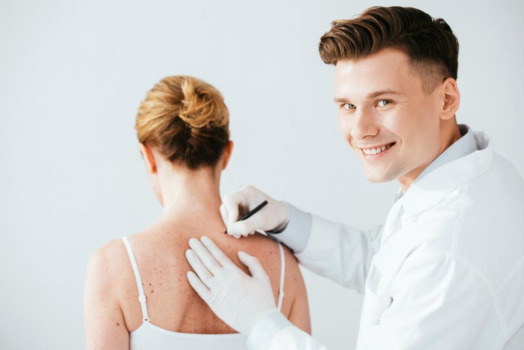 dermatologista alegre em luvas de látex segurando caneta marcador perto da mulher com melanoma isolado no branco
  - Foto, Imagem