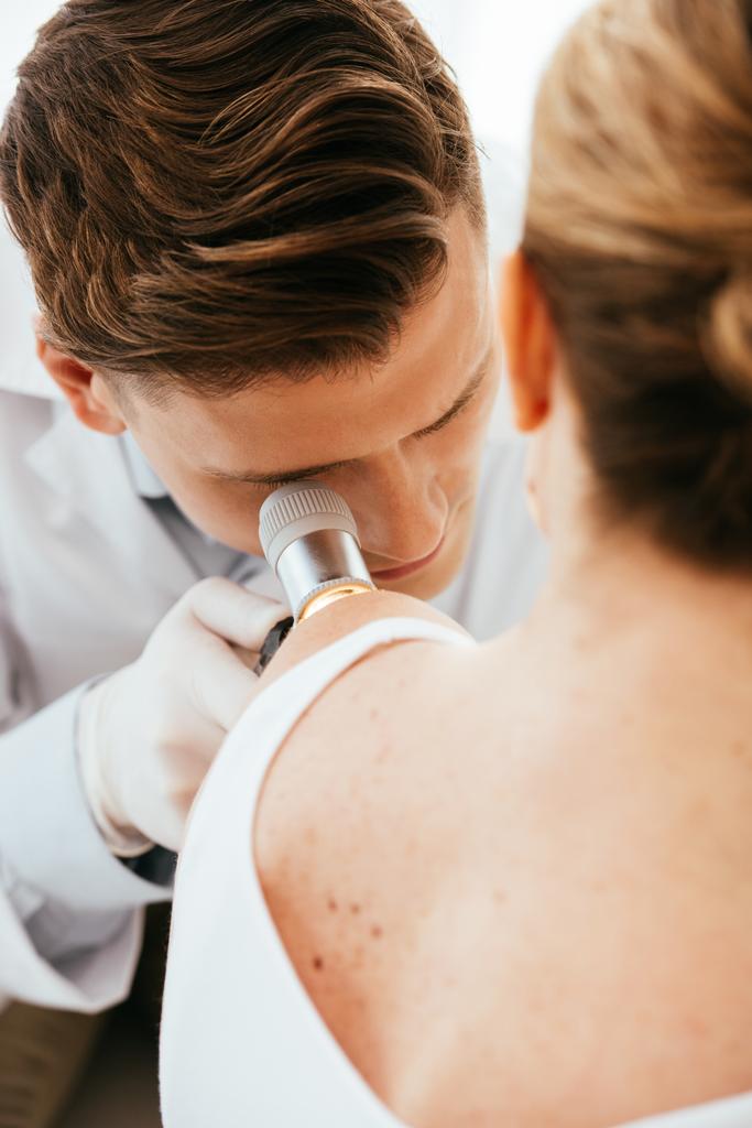 dermatoloog die dermatoscoop houdt tijdens het onderzoeken van patiënt met huidziekte   - Foto, afbeelding