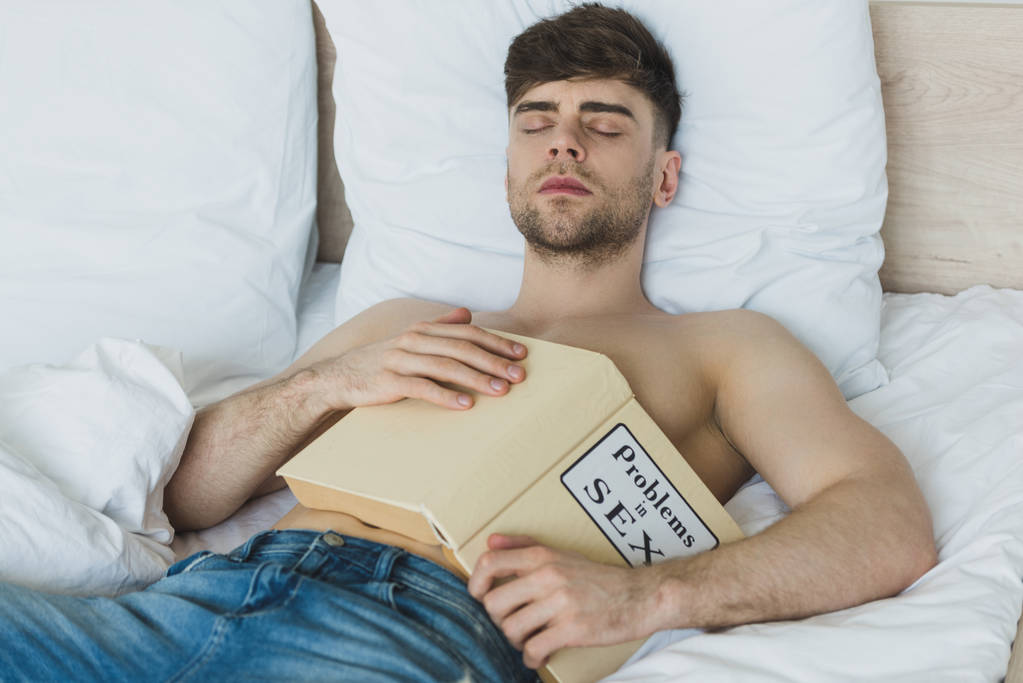 handsome shirtless man in blue jeans sleeping with problems in sex book - Photo, Image
