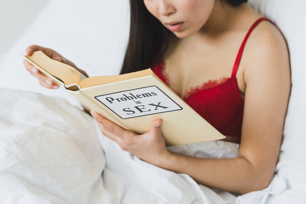 gedeeltelijke weergave van de vrouw in rode beha liggend lezen problemen in seks boek terwijl liggend in bed - Foto, afbeelding